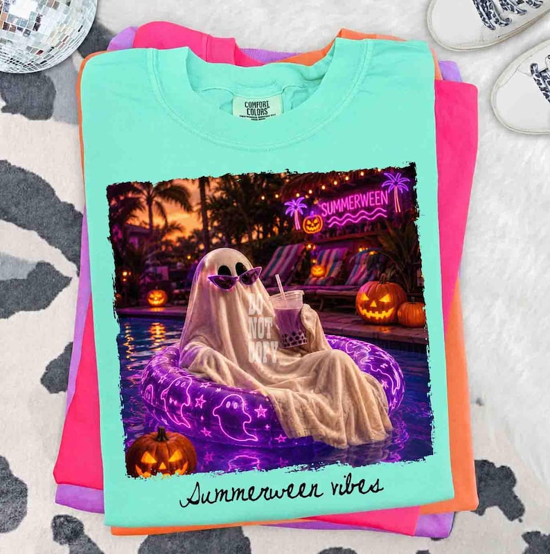 May include: A light teal Comfort Colors t-shirt featuring a graphic of a ghost in sunglasses relaxing in a pool with a drink. The graphic includes the text "Do Not Disturb" and "Summerween vibes". The shirt is stacked with other colorful shirts.