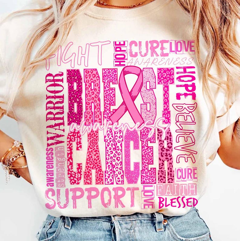 Op de afbeelding: Cr&egrave;mekleurig T-shirt met een roze lint en de woorden "Breast Cancer Awareness" in een roze luipaardprint. Extra woorden zijn "Fight", "Hope", "Cure", "Love", "Warrior", "Support" en "Believe".