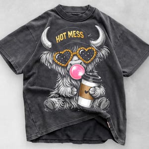 K&ouml;nnte beinhalten: Dunkelgraues T-Shirt mit einem Cartoon-Highland-Rind mit herzf&ouml;rmiger Sonnenbrille, das eine Kaugummiblase bl&auml;st. Das Rind h&auml;lt eine Kaffeetasse und tr&auml;gt einen Hut mit der Aufschrift "HOT MESS".