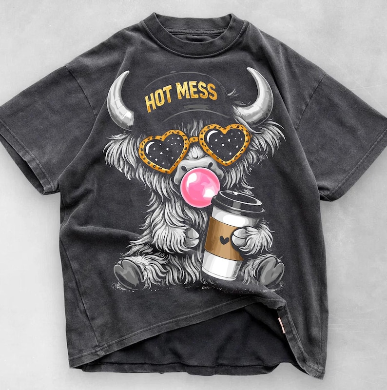 K&ouml;nnte beinhalten: Dunkelgraues T-Shirt mit einem Cartoon-Highland-Rind mit herzf&ouml;rmiger Sonnenbrille, das eine Kaugummiblase bl&auml;st. Das Rind h&auml;lt eine Kaffeetasse und tr&auml;gt einen Hut mit der Aufschrift "HOT MESS".
