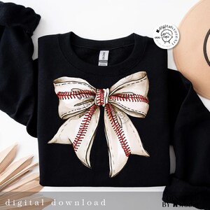May include: Black sweatshirt with a white and red baseball-themed bow on the front. The bow is made of fabric with red stitching that looks like baseball seams.