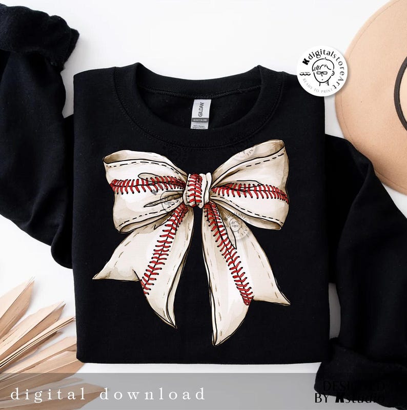 May include: Black sweatshirt with a white and red baseball-themed bow on the front. The bow is made of fabric with red stitching that looks like baseball seams.