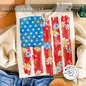 Puede incluir: Una sudadera blanca con un dise&ntilde;o de bandera estadounidense roja, blanca y azul. La bandera est&aacute; decorada con margaritas blancas y flores rojas. El texto "DESIGNED BY Kstudio" est&aacute; en la esquina superior derecha de la imagen.