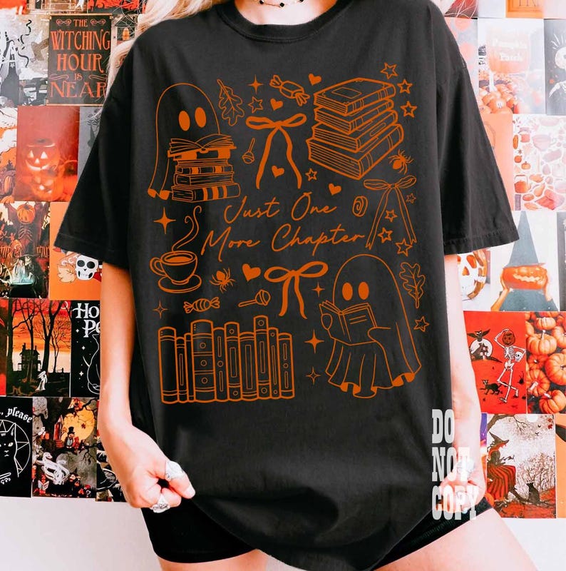 May include: Black t-shirt with an orange graphic featuring ghosts, books, bows, and the text "Just One More Chapter." The design includes a coffee cup, stars, and other Halloween-themed elements. The shirt is a casual, oversized fit.