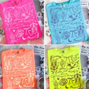 May include: Four t-shirts in pink, blue, orange, and neon green, each with a white graphic. The graphic includes cowboy boots, a cowboy hat, a horseshoe, and the text "Boots and bling it's a Cowgirl thing" and "Cow Girl".