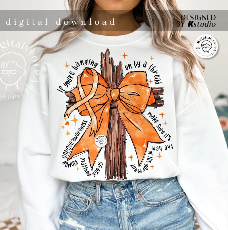 May include: White sweatshirt with an orange ribbon tied around a brown wooden cross. The text "If you're hanging on by a thread make sure it's the hem of His garment" is printed on the sweatshirt.  Cancer awareness, Matthew 9:20-22, and KIDNEY are also printed on the sweatshirt.