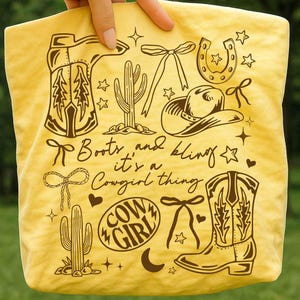 May include: Yellow tote bag with brown illustrations of cowboy boots, a cowboy hat, cactus, horseshoe, and bows. Text reads "Boots and bling it's a Cowgirl thing" and "Cowgirl".