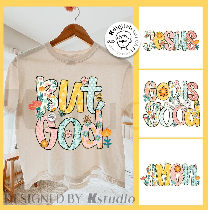 May include: A beige t-shirt with the phrase "But God" in colorful, floral-decorated letters. The design includes the words "Jesus", "God is Good", and "Amen" in a similar style. The shirt is hanging on a wooden hanger.