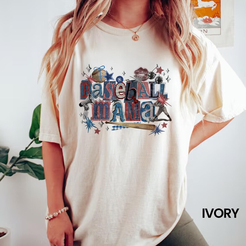 K&ouml;nnte beinhalten: Elfenbeinfarbenes T-Shirt mit Baseball-Motiv. Die Grafik zeigt die Worte "Baseball Mama" in einer Mischung aus roten, blauen und grauen Schriftarten sowie Baseball-Illustrationen. Das Shirt ist ein bequemer, l&auml;ssiger Stil.