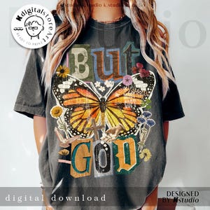 Può includere: T-shirt grigio scuro con un disegno a farfalla e le parole "BUT GOD". La farfalla ha ali arancioni, nere e bianche, circondata da fiori e una croce. Le parole "digital download" sono in basso. Progettato da Mstudio.