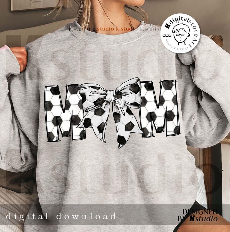Peut inclure: Un sweat-shirt gris avec un motif de ballon de football noir et blanc qui &eacute;pelle "MOM" avec un grand n&oelig;ud noir et blanc au milieu.
