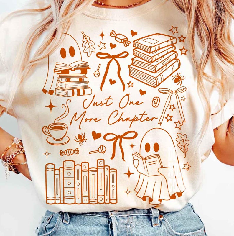 May include: Cream-colored t-shirt with a brown graphic design featuring books, ghosts, bows, and the text "Just One More Chapter." The design includes a coffee cup, stars, and candy, creating a cozy, book-themed aesthetic.