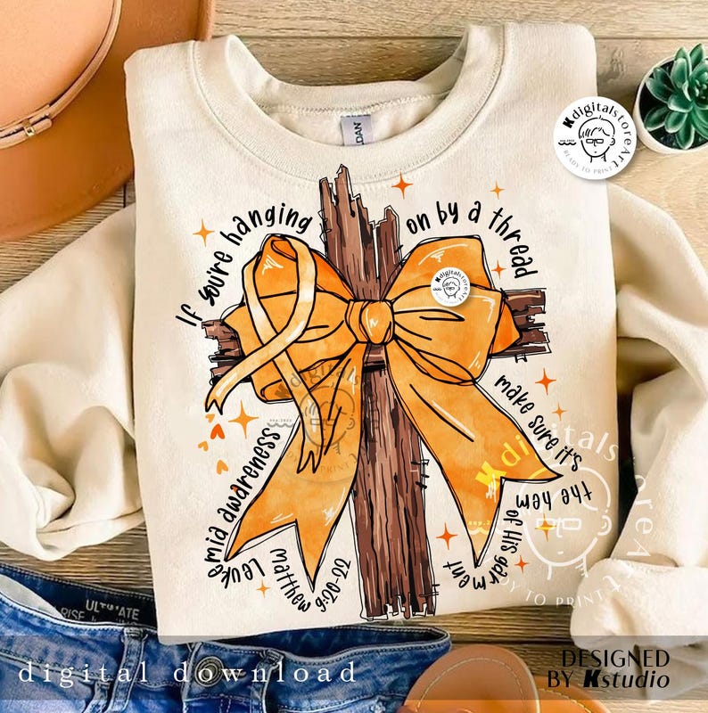 May include: A beige sweatshirt featuring a brown wooden cross with an orange ribbon. The text "If you're hanging on by a thread make sure it's the hem of His garment" is printed on the sweatshirt.