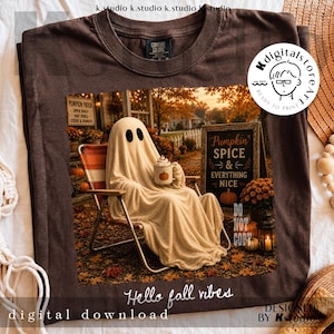 May include: Brown t-shirt with a fall-themed graphic. A ghost figure is depicted relaxing in a chair, holding a pumpkin spice latte. The image includes the text "Pumpkin Spice & Everything Nice" and "Hello fall vibes".