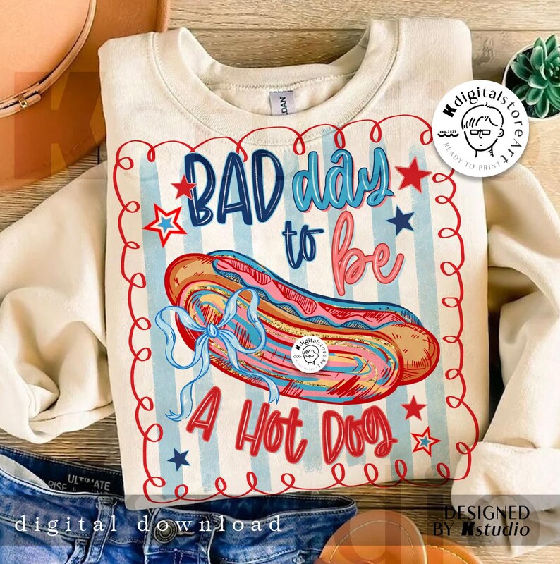 May include: Cream-colored sweatshirt with a graphic of a hot dog and the text "BAD day to be A Hot Dog." The design includes red, white, and blue elements, with a decorative border and stars. The sweatshirt is a digital download.