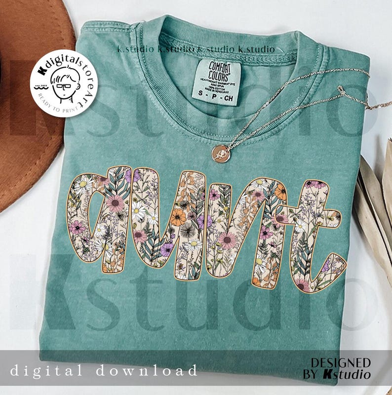 May include: A teal t-shirt with a floral design that spells out "aunt". The design is in a light brown outline with a variety of flowers and leaves in shades of pink, purple, yellow, and green.