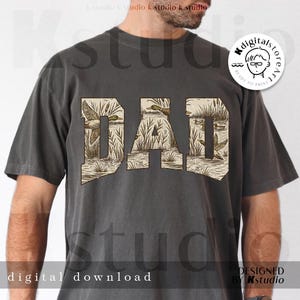 May include: Dark gray t-shirt with the word "DAD" in a tan, vintage-style font. The letters are filled with a duck hunting scene. The shirt also has the words "digital download" and "designed by Kstudio".