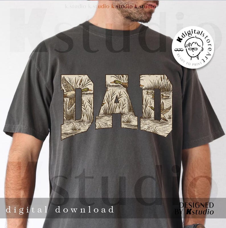 May include: Dark gray t-shirt with the word "DAD" in a tan, vintage-style font. The letters are filled with a duck hunting scene. The shirt also has the words "digital download" and "designed by Kstudio".