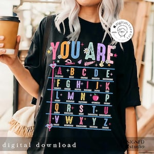 May include: Black t-shirt with a colorful graphic that says "You Are" and lists positive adjectives for each letter of the alphabet.
