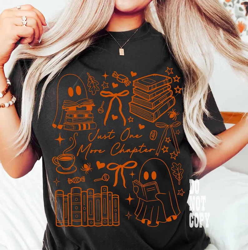 May include: Black t-shirt with orange graphic illustrations of books, ghosts, bows, and stars. The text "Just One More Chapter" is also in orange. The shirt is a comfortable, casual style.