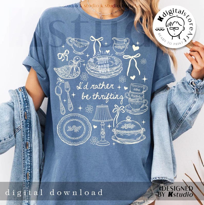 May include: Blue t-shirt with a white graphic design featuring teacups, plates, a duck, and the text "I'd rather be thrifting." The shirt also has the text "digital download" and "designed by Kstudio."