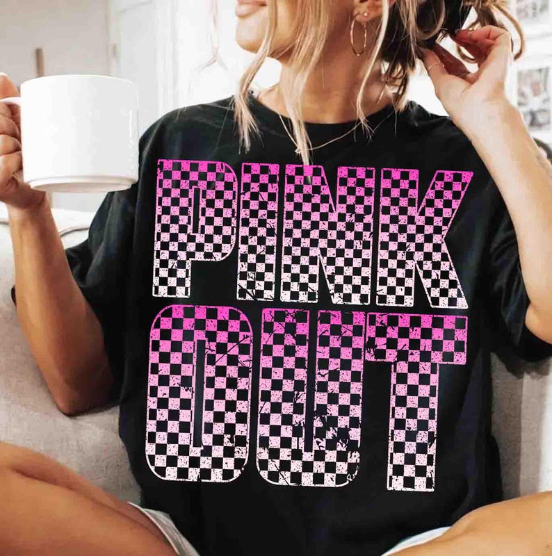 May include: Black t-shirt with the words "PINK OUT" in large, checkered pink and white letters. The shirt has a distressed, vintage look. The person in the image is holding a white mug.