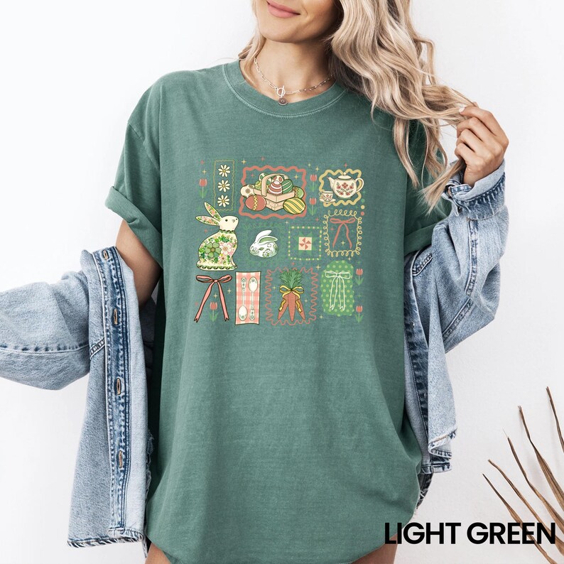 May include: Light green t-shirt featuring a colorful Easter-themed graphic. The design includes framed illustrations of a bunny, eggs, carrots, and other spring elements. The text "LIGHT GREEN" is printed at the bottom.