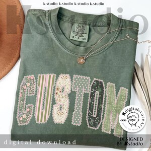 May include: An olive green t-shirt with the word "CUSTOM" in a floral design. The letters are filled with various patterns, including stripes, polka dots, and floral prints. A gold necklace with a pendant rests on the shirt. The text "digital download" is at the bottom.
