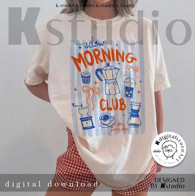 May include: Cream-colored t-shirt with a "Slow Morning Club" design featuring coffee-related illustrations in orange and blue. The design includes a coffee maker, grinder, and a cup of coffee. The shirt is a digital download.
