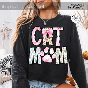 May include: Black sweatshirt with a pink and white floral design that says "Cat Mom" with a pink bow on the "T".