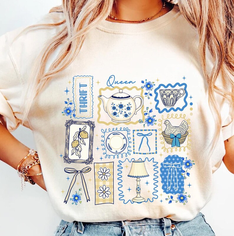 May include: Cream-colored sweatshirt featuring a collage of vintage-style illustrations in blue and yellow. Designs include a teapot, teacup, lemons, a chicken in a basket, and the word "Thrift". The word "Queen" is also present.