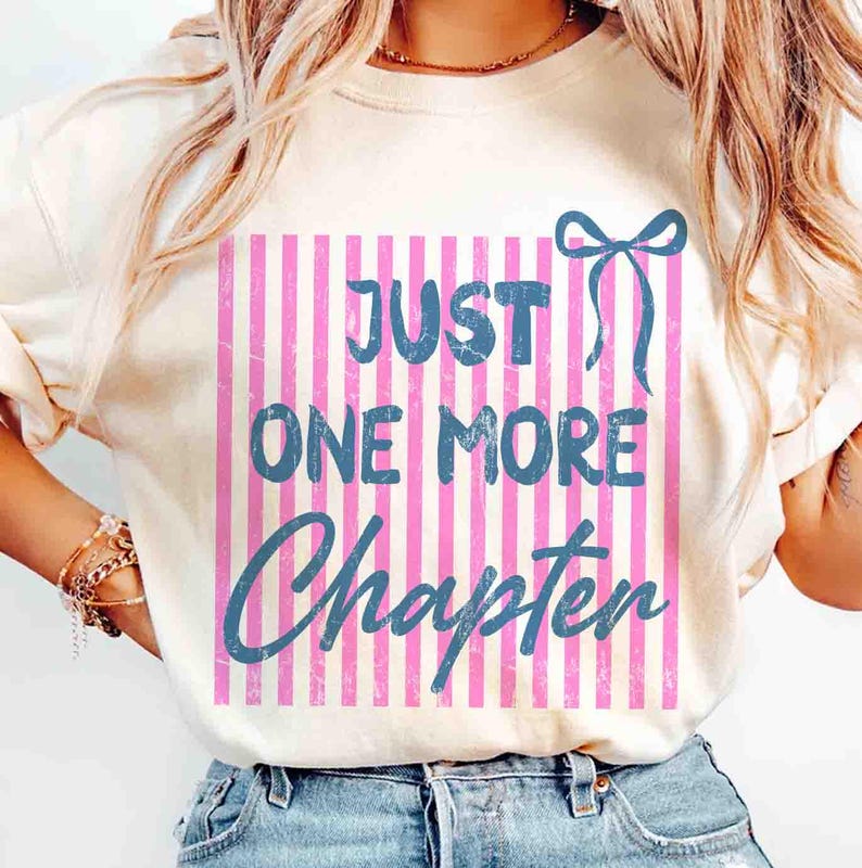 Puede incluir: Camiseta color crema con el texto azul "JUST ONE MORE CHAPTER". El texto est&aacute; sobre un fondo de rayas rosas y blancas, con un lazo azul. La camiseta es de estilo casual.