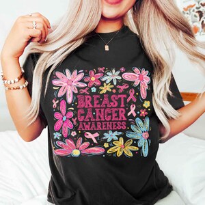 May include: Black t-shirt with a floral design and the words "Breast Cancer Awareness" in pink. The flowers are in shades of pink, blue, yellow, and green, with pink ribbons throughout the design.