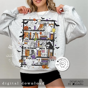 May include: Light gray sweatshirt featuring a Halloween-themed bookshelf design. The graphic includes ghosts, pumpkins, books, and spiderwebs. The text "digital download" is at the bottom. The design is in shades of orange, purple, black, and white.