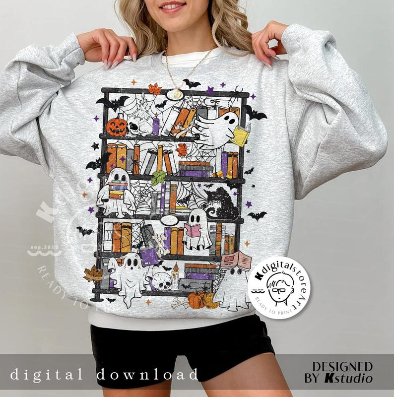 May include: Light gray sweatshirt featuring a Halloween-themed bookshelf design. The graphic includes ghosts, pumpkins, books, and spiderwebs. The text "digital download" is at the bottom. The design is in shades of orange, purple, black, and white.