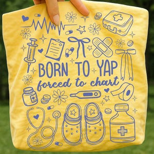 K&ouml;nnte beinhalten: Gelbe Tragetasche mit blauen medizinischen Illustrationen, darunter ein Stethoskop, eine Spritze und Clogs. Der Text "BORN TO YAP forced to chart" ist aufgedruckt. Die Tasche wird von einer Hand gehalten.