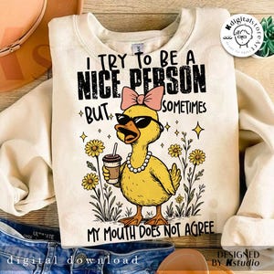 May include: A cream-coloured sweatshirt featuring a yellow duck wearing sunglasses, a pink bow, and a pearl necklace, holding a coffee cup. The text reads "I TRY TO BE A NICE PERSON BUT SOMETIMES MY MOUTH DOES NOT AGREE."