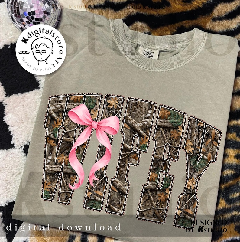 Puede incluir: Camiseta verde salvia con la palabra "Wifey" en un patr&oacute;n de camuflaje y un lazo rosa. Las palabras "digital download" est&aacute;n en la parte inferior de la camiseta.