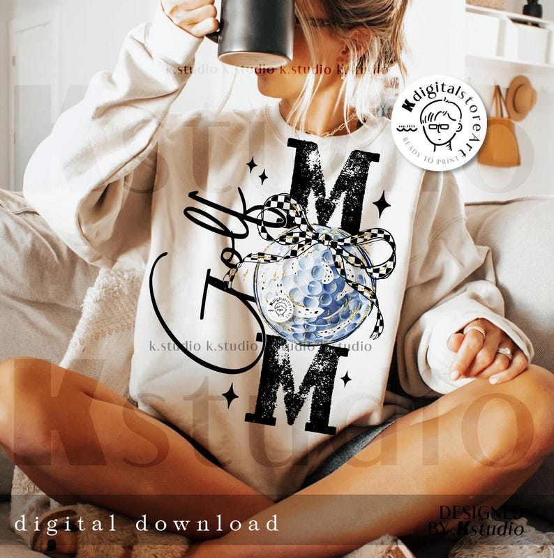 May include: A cream-colored sweatshirt with the word "MOM" in large black letters. A golf ball design is featured in the center, with a black and white checkered ribbon. The words "Golf Mom" are written in a script font.