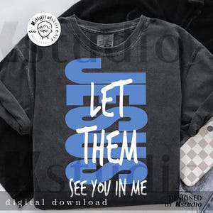 May include: A dark gray sweatshirt with the words "LET THEM SEE YOU IN ME" in white and blue block letters. The words are stacked vertically. The phrase "digital download" is at the bottom.