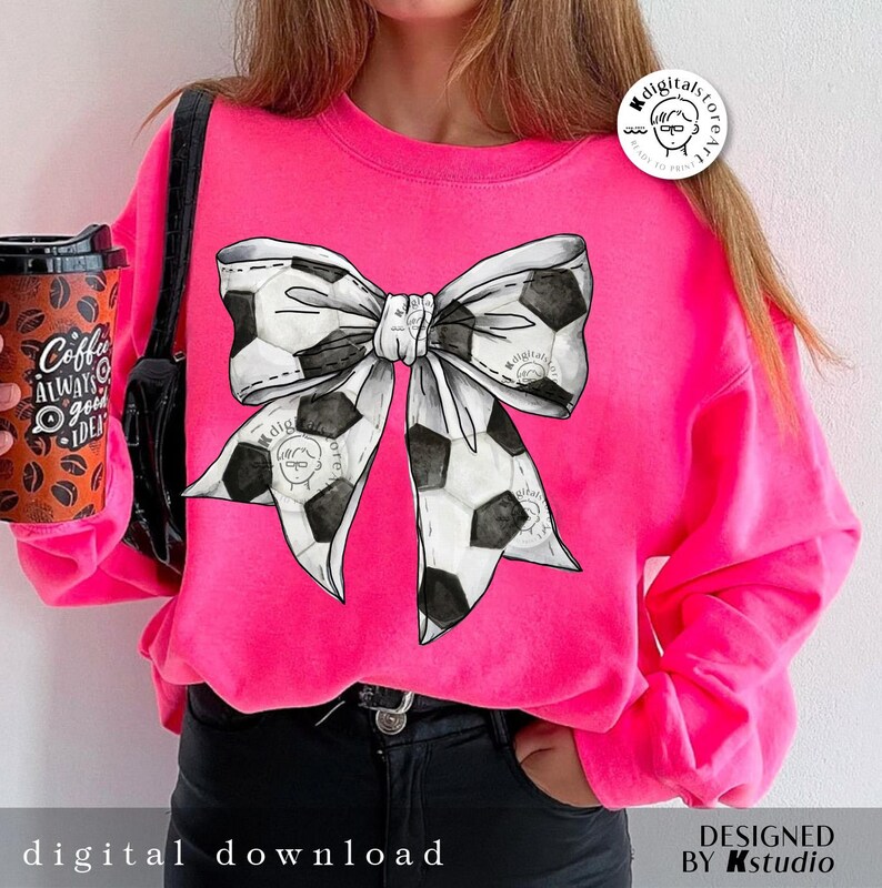 May include: A pink sweatshirt with a black and white soccer ball bow design. The sweatshirt has a crew neck and long sleeves.