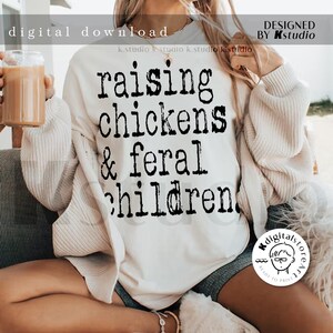 May include: A white sweatshirt with black text that reads "raising chickens & feral children".