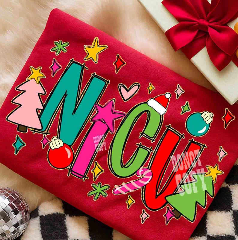 May include: A red sweatshirt with the word "NICU" in colorful, festive lettering. The letters are decorated with Christmas-themed graphics, including stars, ornaments, and a candy cane. A gift box with a red bow is in the background.