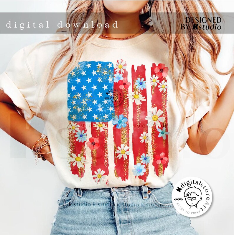 Puede incluir: Una camiseta blanca con un dise&ntilde;o de bandera estadounidense desgastada con rayas y estrellas rojas, blancas y azules. La bandera est&aacute; decorada con flores blancas y azules. El texto "DESIGNED BY Kstudio" est&aacute; en la esquina superior derecha de la imagen.