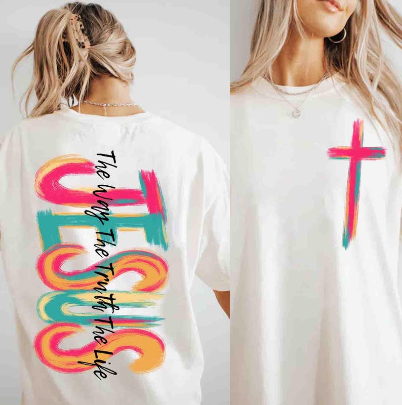 May include: White t-shirt with a colorful cross graphic on the front and the word "JESUS" vertically on the back, with the text "The Way The Truth The Life". The graphics are in shades of pink, teal, yellow, and orange.