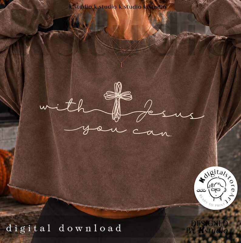 Op de afbeelding: Een bruin, langmouwige, cropped sweatshirt met een witte afbeelding van een krabbelkruis en de tekst "with Jesus you can." Het kledingstuk heeft een ronde hals, lange mouwen en een zoom met een rafelige rand, met een vervaagde afwerking.
