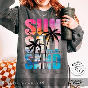May include: A gray sweatshirt with a colorful graphic design that says "SUN SALT SAND" with palm trees and a sunset. The graphic is in a rainbow color scheme with pink, orange, yellow, blue, and green.
