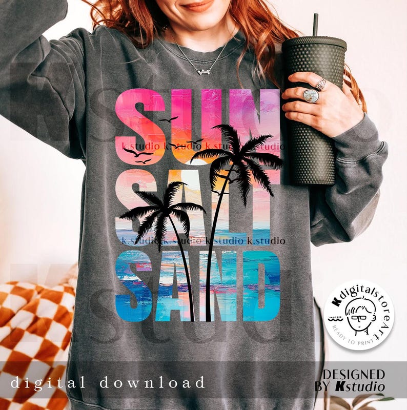May include: A gray sweatshirt with a colorful graphic design that says "SUN SALT SAND" with palm trees and a sunset. The graphic is in a rainbow color scheme with pink, orange, yellow, blue, and green.