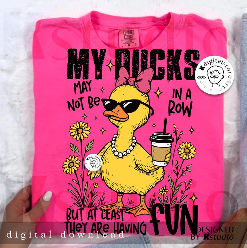 Puede incluir: Camiseta rosa intenso con un gr&aacute;fico de un pato amarillo con gafas de sol, un collar de perlas y un lazo rosa. El pato sostiene una taza de caf&eacute;. El texto dice "MY DUCKS MAY NOT BE IN A ROW BUT AT LEAST THEY ARE HAVING FUN."