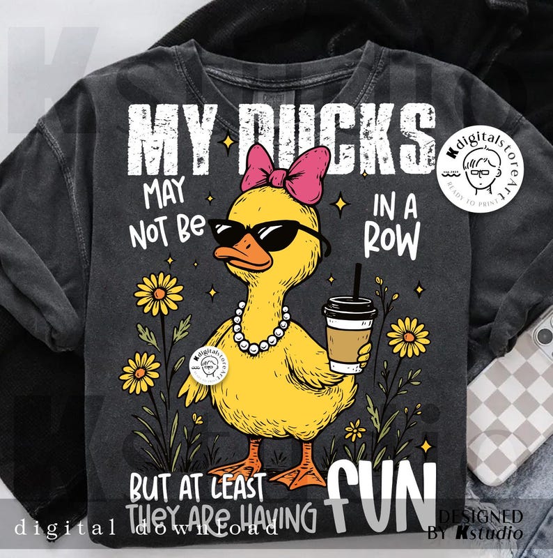 Puede incluir: Sudadera gris oscuro con un gr&aacute;fico de un pato amarillo con gafas de sol, un lazo rosa y un collar de perlas. El texto dice: "MY DUCKS MAY NOT BE IN A ROW BUT AT LEAST THEY ARE HAVING FUN."